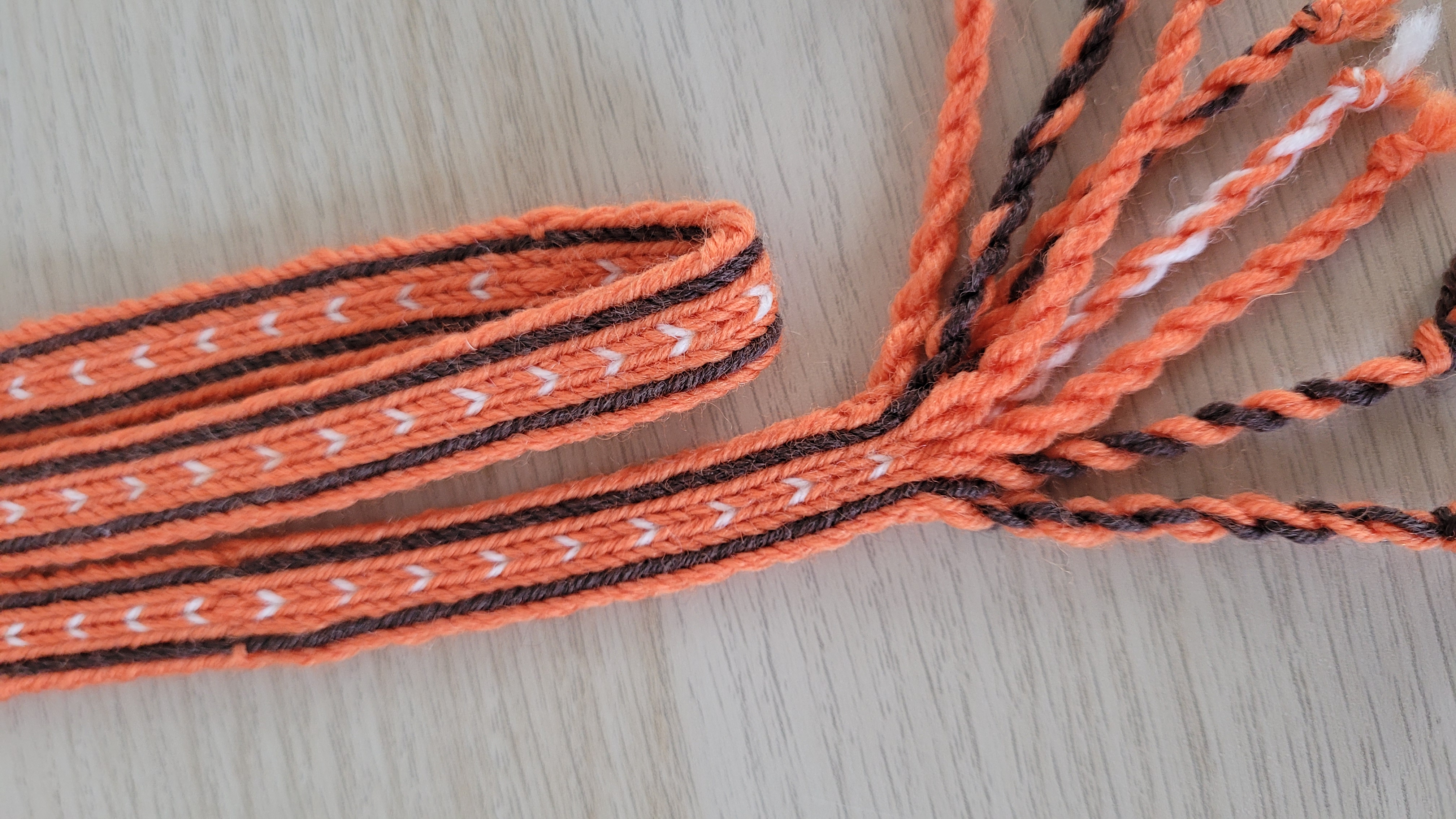 Brettchengewebter Bortengürtel mit Herzchenmuster Orangene Brettchenborte mit gedrehten Fransen.