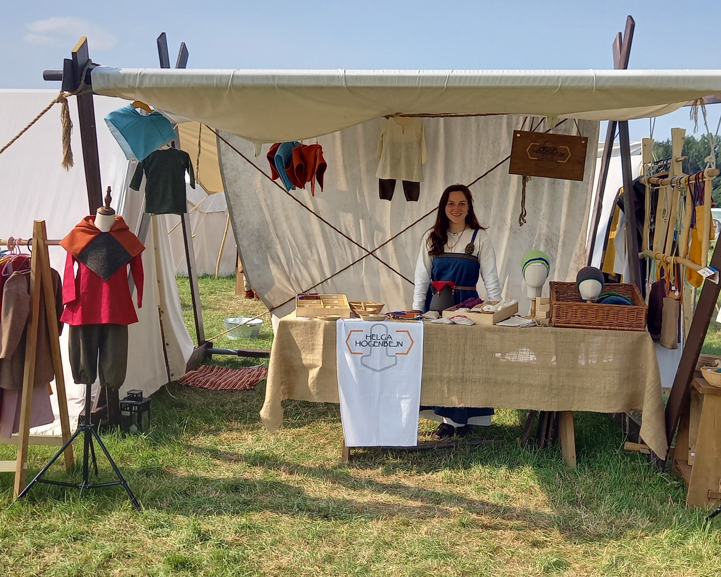 Marktstand Helga Hogenbejn Mittelalter Marktstand mit Kinderkleidung und Frau hinter einem Tisch.